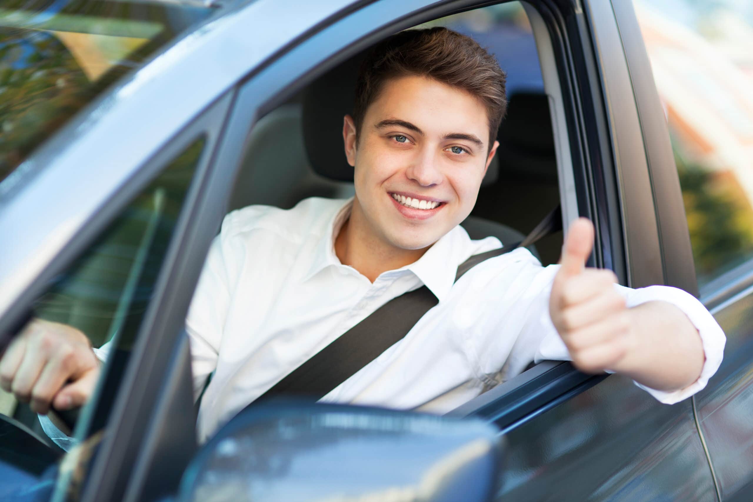 Smilende gutt som sitter i bilen med vinduet nede, hånden ut og tommel opp
